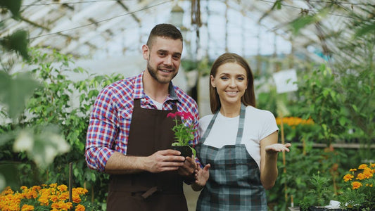 Happy gardeners holding a plant together in a lush greenhouse setting.